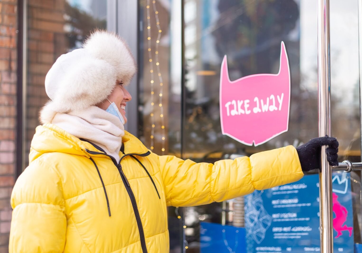 Happy young woman at the door of the restaurant on a cold winter day, lettering, takeaway food. Happy young woman at the door of the restaurant on a cold winter day, lettering, takeaway food.
